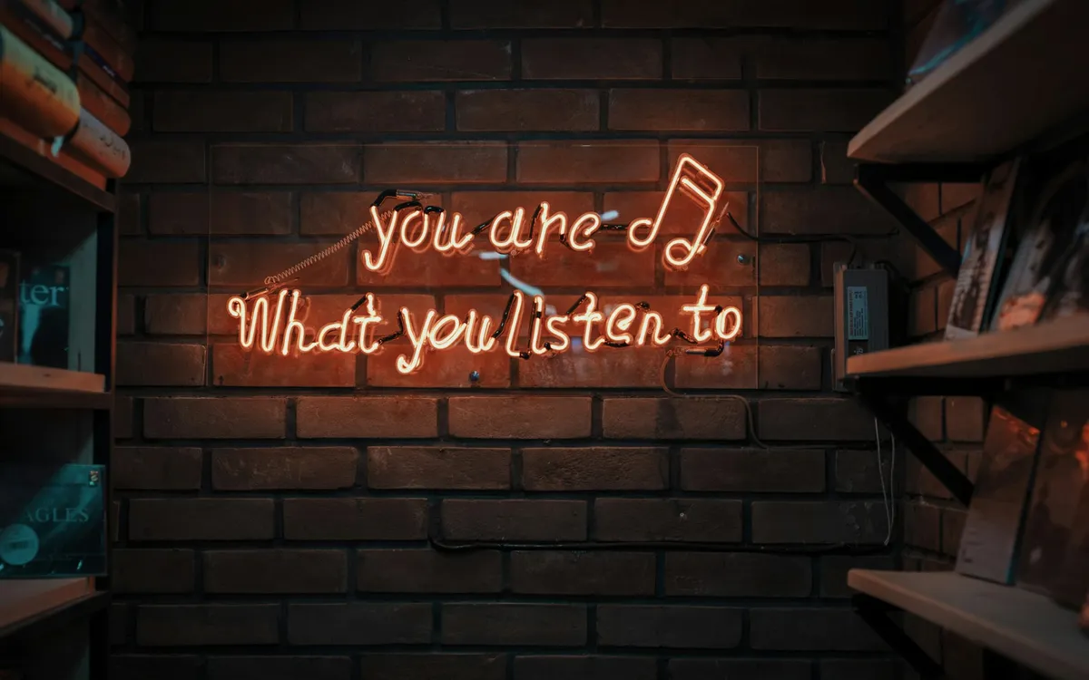 Placeholder: a neon sign on a brick wall that reads “you are what you listen to”.
