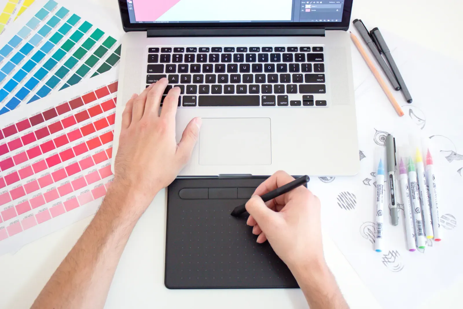 Placeholder: hands drawing on a tablet beside a laptop and colour swatches.